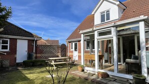 A house with a patio, a wooden table, and a glass door leading to a covered outdoor area. - Bilbo's Cottage, Sheringham (Sheringham)