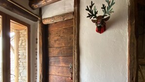 Una puerta de madera rústica, una pared de piedra, un banco con cojín y un adorno de cabeza de ciervo en la pared.