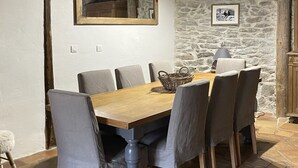 Un comedor con mesa de madera y sillas tapizadas en gris, una pared de piedra y armarios de madera.