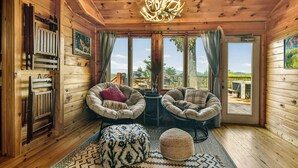 A cozy cabin interior with wooden walls, two cushioned chairs, a patterned rug, and a chandelier.