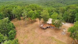A cabin surrounded by dense forest with a deck and a fire pit area.