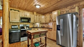 A wooden-paneled kitchen with a refrigerator, microwave, stove, and wooden cabinets.