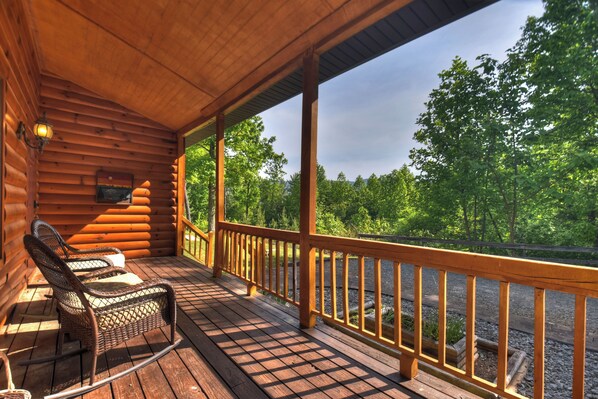 Terraza de madera con sillas de mimbre y barandilla con vistas a un bosque.