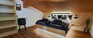 Un dormitorio con techo de madera, una cama con almohadas, una silla y una mesita con una planta.