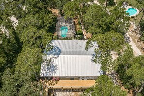 Une vue aérienne d’une maison entourée d’arbres, avec une piscine et une terrasse couverte.