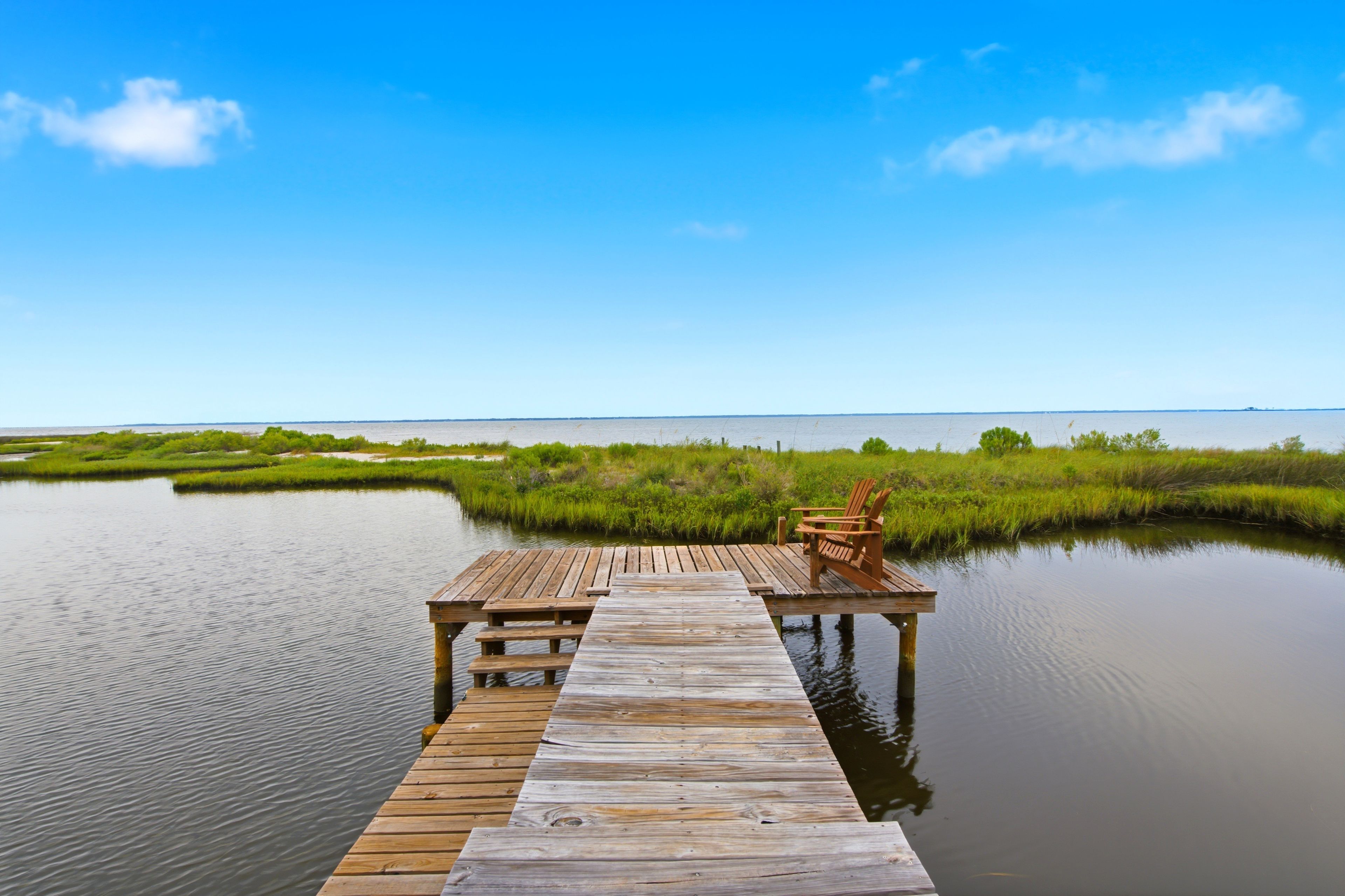 A wooden pier extending into calm water with a chair at the end, surrounded by lush greenery.