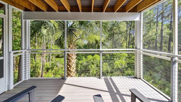 Une terrasse extérieure couverte, dotée de poutres en bois et de panneaux de verre, qui offre une vue sur une forêt luxuriante.