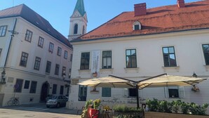 A building with a green spire, a café with outdoor seating, and a parked car. - Room-quiet Single Bedroom in the Centre (Zagreb)