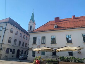A building with a green spire, a café with outdoor seating, and a parked car. - Room-quiet Single Bedroom in the Centre (Zagreb)