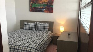 Una habitación de hotel con cama, mesita de noche, lámpara y un cuadro en la pared.
