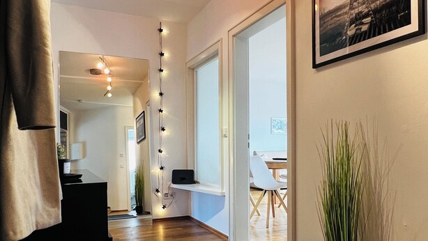 Ein modernes Interieur mit Holzboden, einem schwarzen Tisch, einem Blumentopf und einem gerahmten Bild an der Wand.