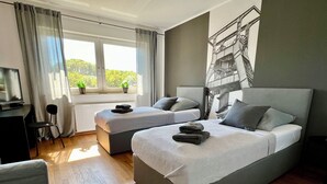 Ein modernes Hotelzimmer mit zwei Betten, einem Schreibtisch und einem großen Fenster mit Blick auf Grünflächen.