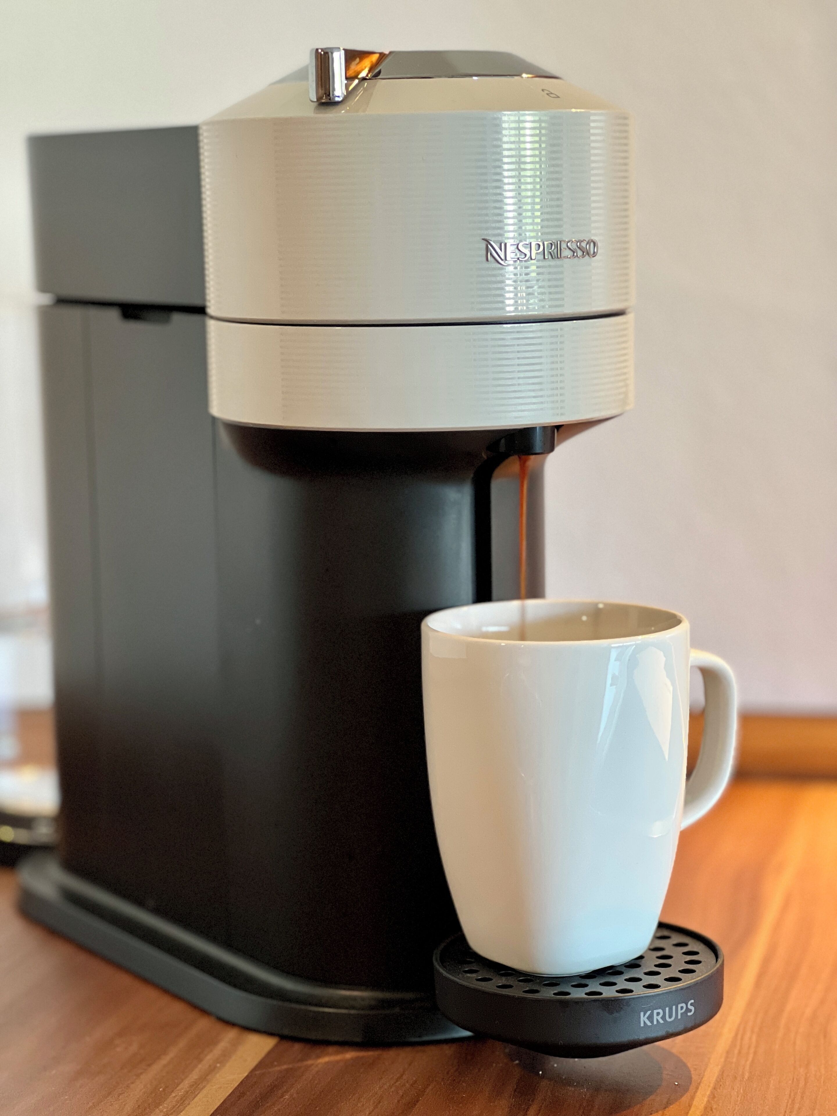 A Nespresso coffee machine with a white cup on a Krups coffee warmer.