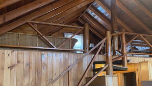 A wooden interior with a staircase leading to a loft area, a sign indicating 'Cairns Island', and a small black object on the floor.