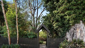 A wooden gate with a house number sign, surrounded by trees and a gravel path.