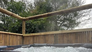 A hot tub with a wooden deck and a wooden fence in the background.