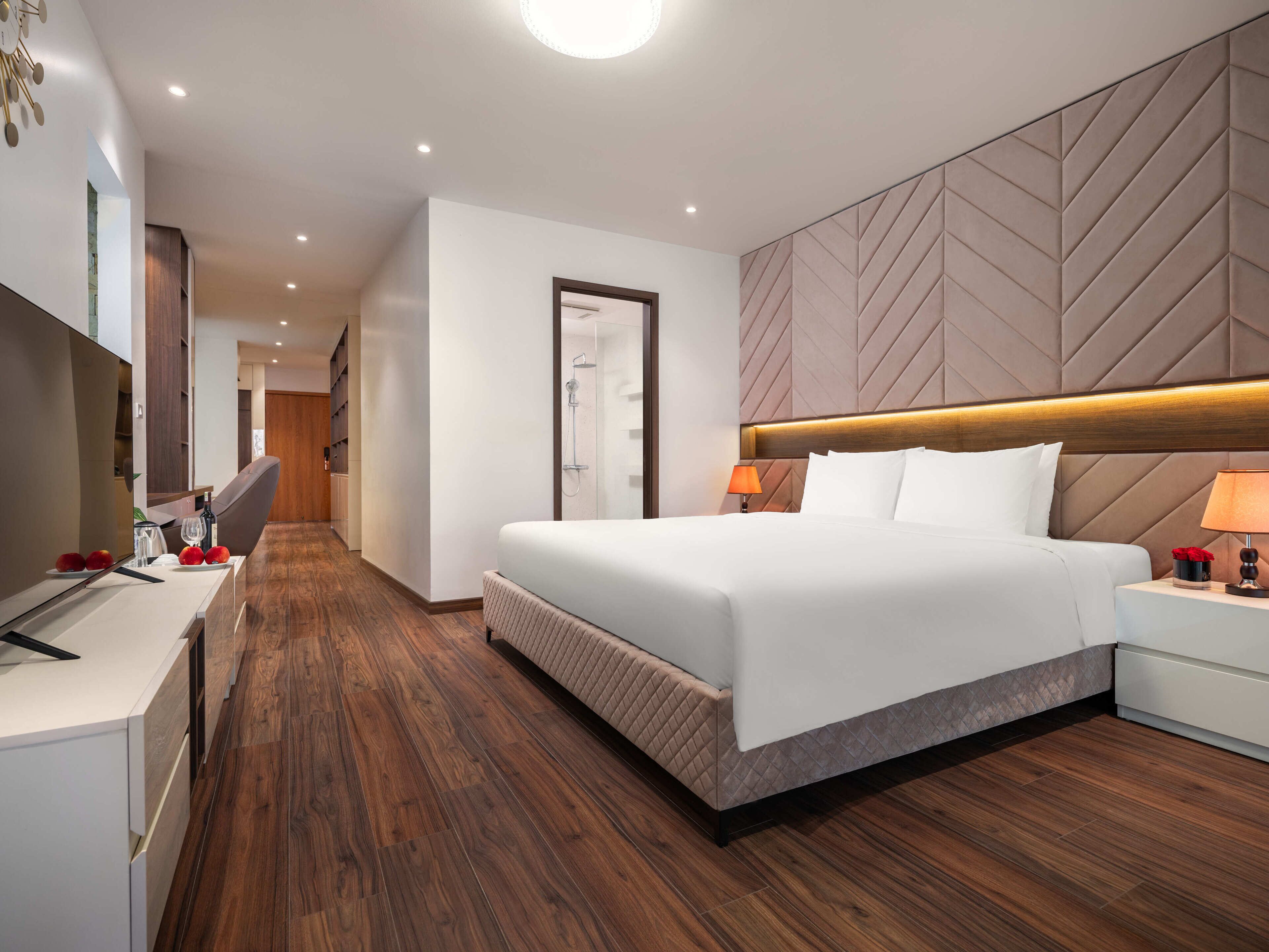 Een moderne hotelkamer met een groot bed, een bureau met stoel, een douche en een houten vloer.