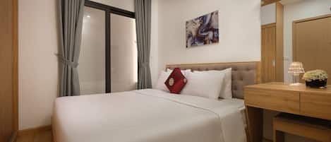 A hotel room with a bed, a wooden desk, a lamp, and a painting on the wall.