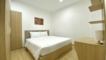 A bedroom with a bed, a wooden wardrobe, a desk with a lamp, and a painting on the wall.