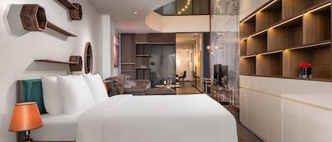 Habitación de hotel moderna con una cama grande, zona de estar, comedor e interior bien iluminado.