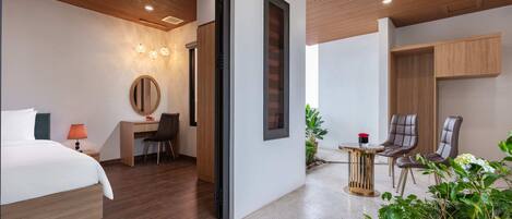 A modern hotel room with a bed, desk, and chairs, a large mirror, and a small balcony with plants.