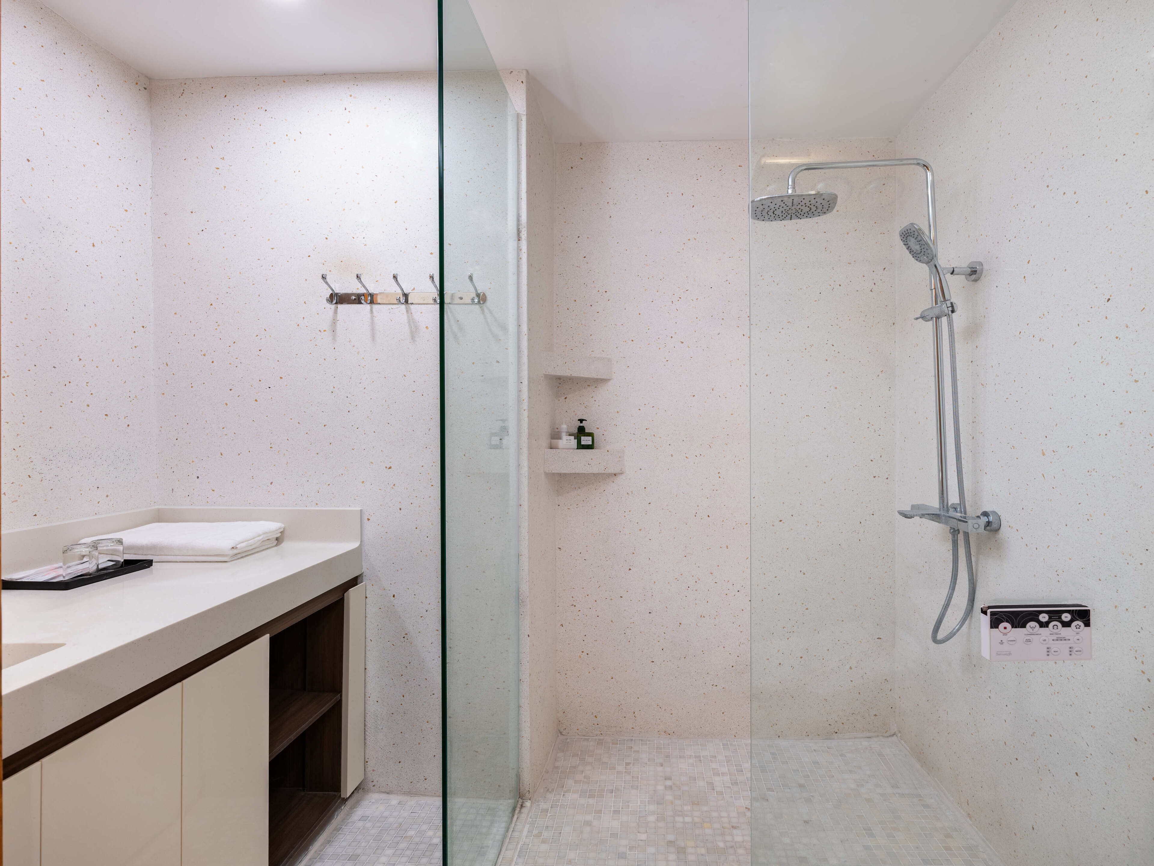 A modern bathroom with a glass-enclosed shower, a white sink with a towel, and a small shelf with toiletries.