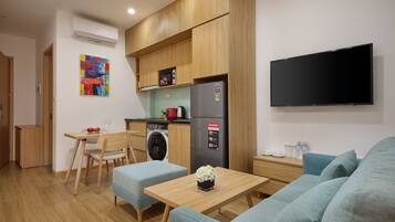 A compact kitchen with wooden cabinets, a washing machine, a refrigerator, and a flat-screen TV.