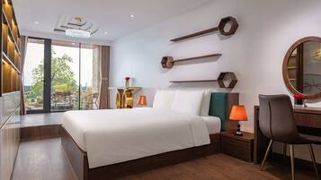 A modern hotel room with a large bed, a desk with a chair, a round mirror, and a view of the outdoors.