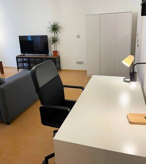 Ett modernt vardagsrum med en soffa, en tv, ett skrivbord med en lampa och en garderob.