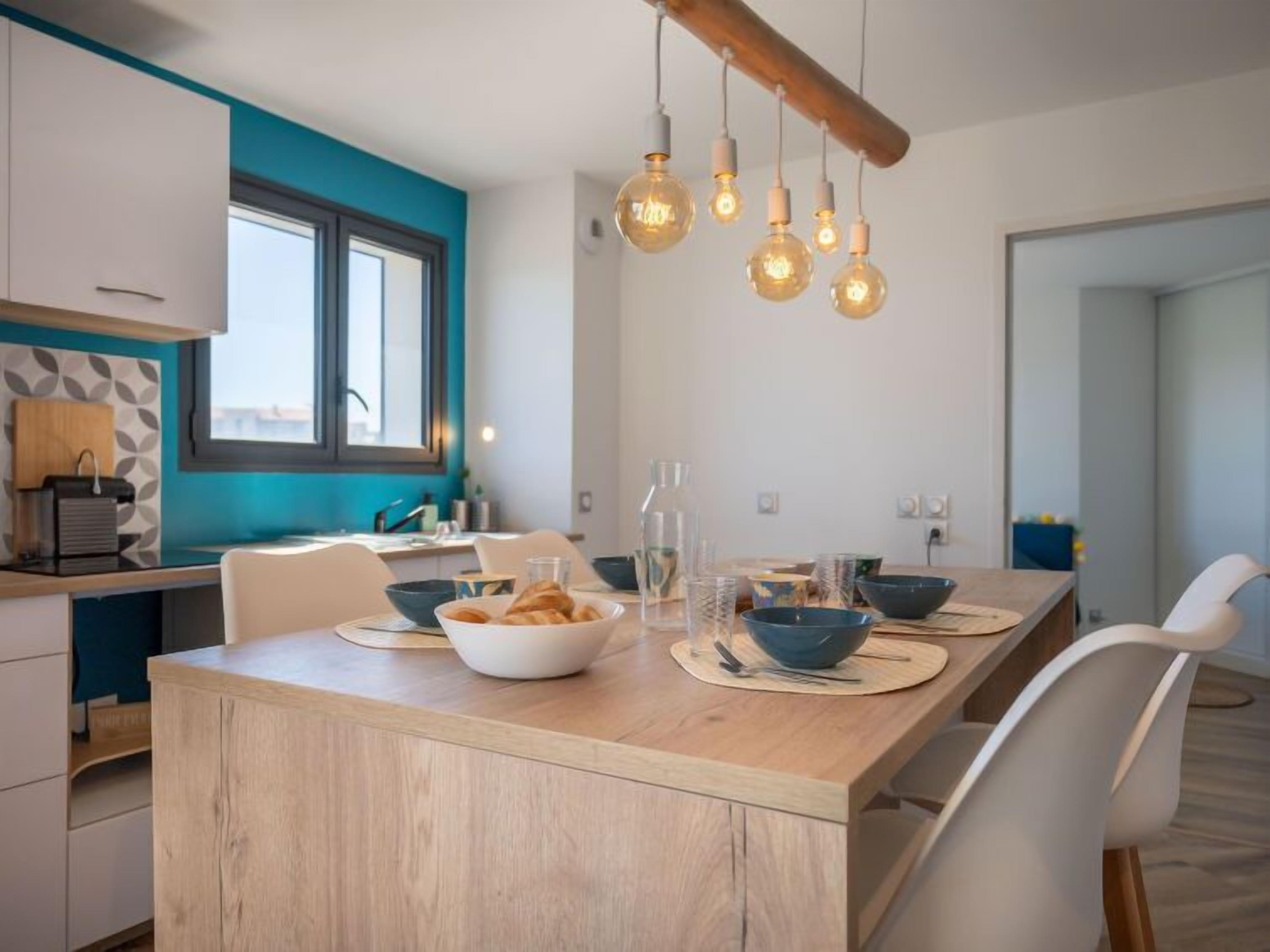 Una cocina moderna con una isla de madera, sillas blancas y lámparas colgantes.