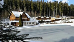 Un complejo turístico con cabañas de madera, terreno cubierto de nieve y un bosque denso al fondo.