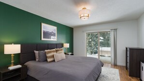 Ein Schlafzimmer mit einem großen Bett, zwei Nachttischen mit Lampen, einem gerahmten Bild an der Wand und Blick auf eine verschneite Landschaft durch eine Schiebetür.