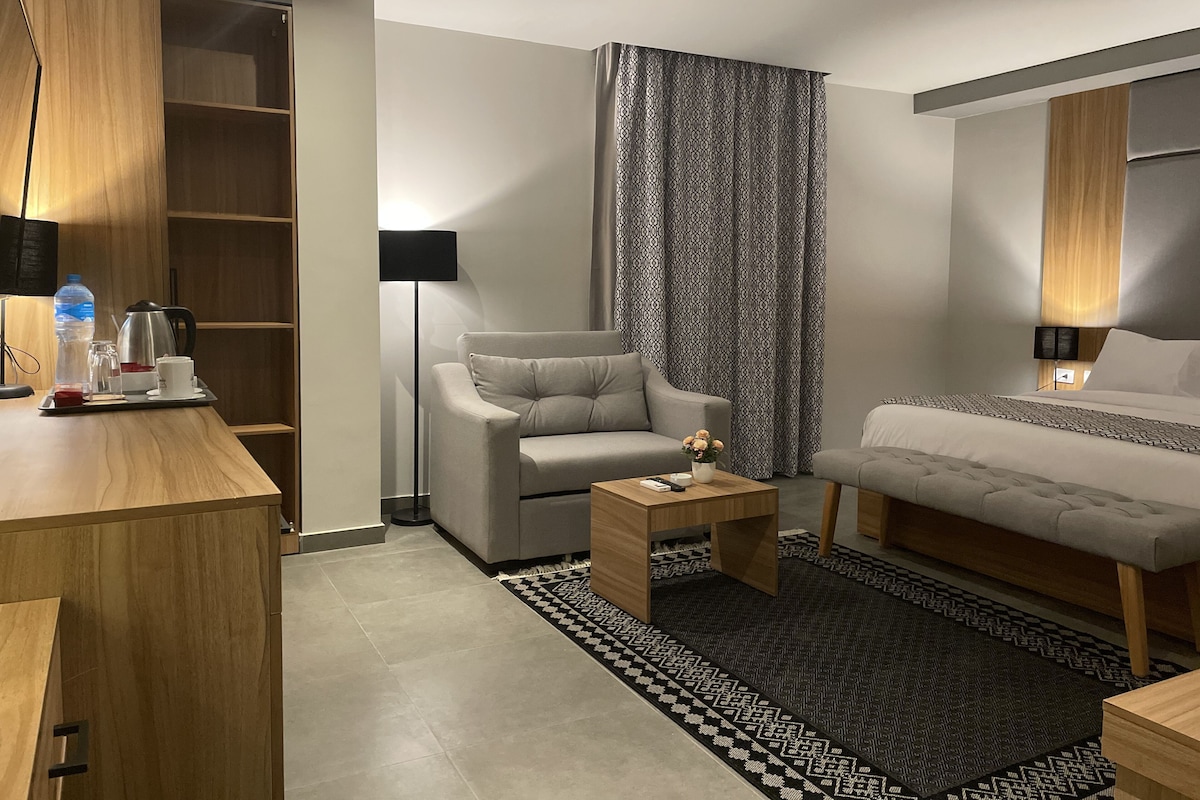 A modern hotel room with a sofa, a bed, a coffee table, a desk, and a wardrobe.