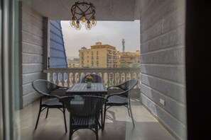 Un balcon avec une table et des chaises, un luminaire décoratif et une vue sur les bâtiments en arrière-plan.