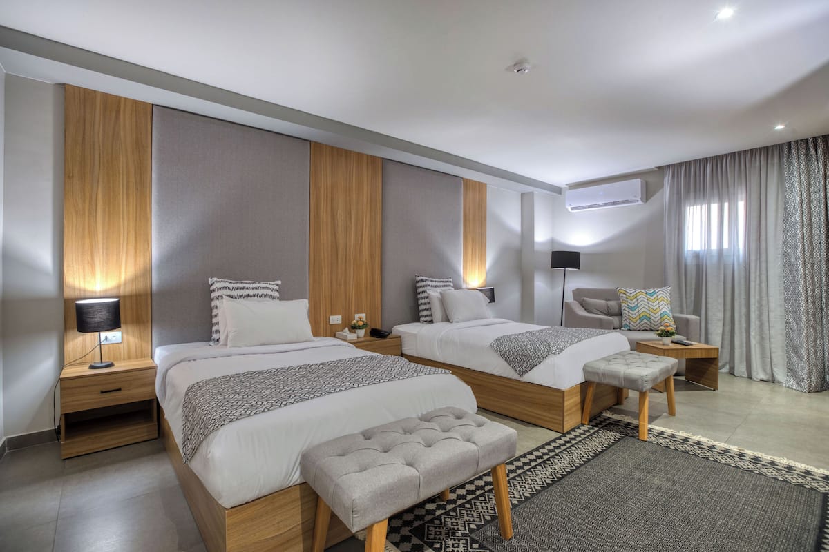 Et moderne hotelværelse med to senge, en sofa, et lille bord og en lampe.