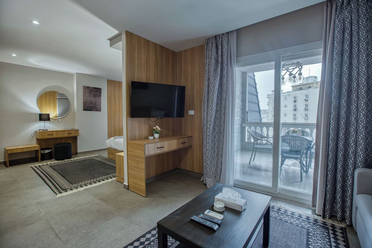 Et moderne hotelværelse med et træskrivebord, et fladskærms-tv, en sofa og en balkon med havemøbler.
