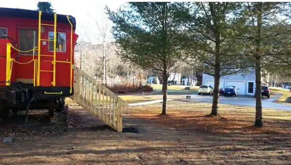 Train car sits adjacent to a wooden bridge in a residential area.