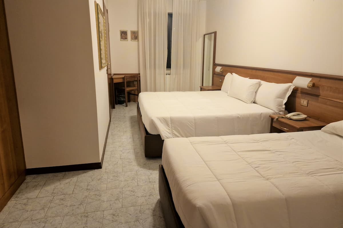 A hotel room with two beds, a desk, a chair, and a bathroom.