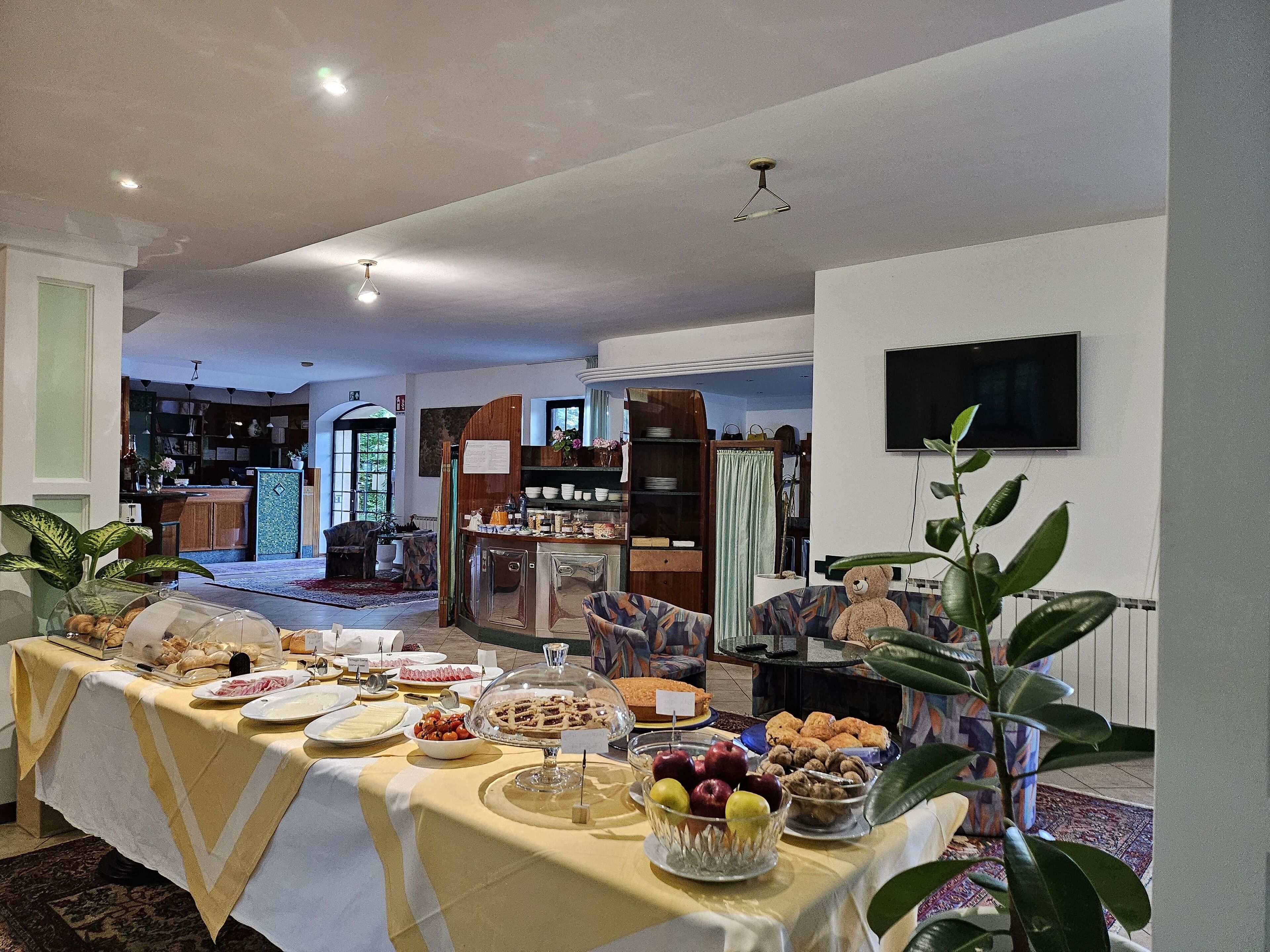 A dining area with a buffet table covered with a yellow tablecloth, featuring various food items and a glass dome covering a dish.