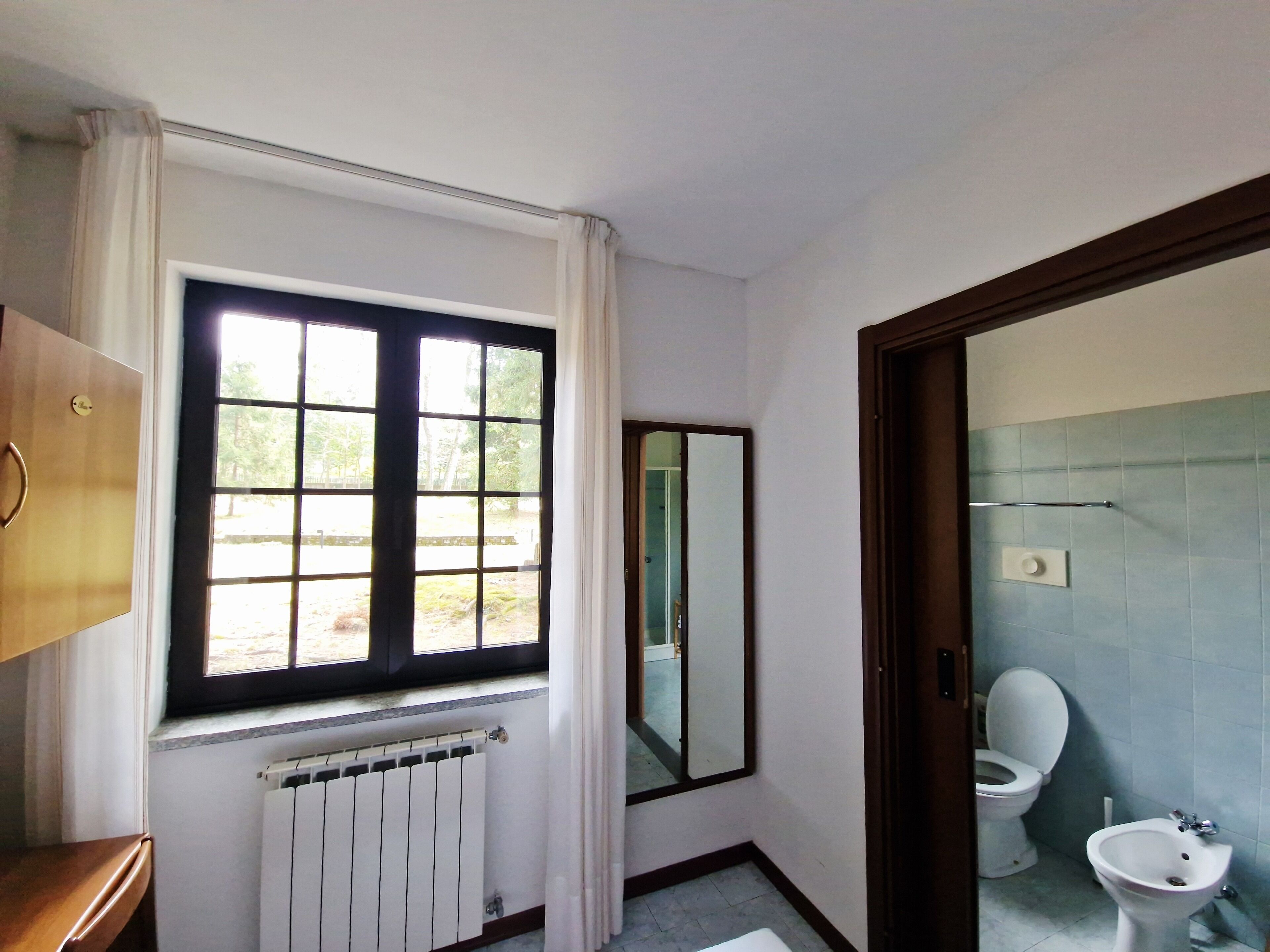 A bathroom with a window, a radiator, a toilet, and a bidet.