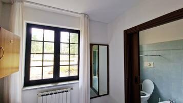 A bathroom with a window, a radiator, a toilet, and a bidet.