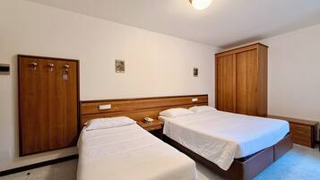 Habitación de hotel con dos camas individuales, armarios de madera, una mesita de noche con lámpara y un aplique de techo.
