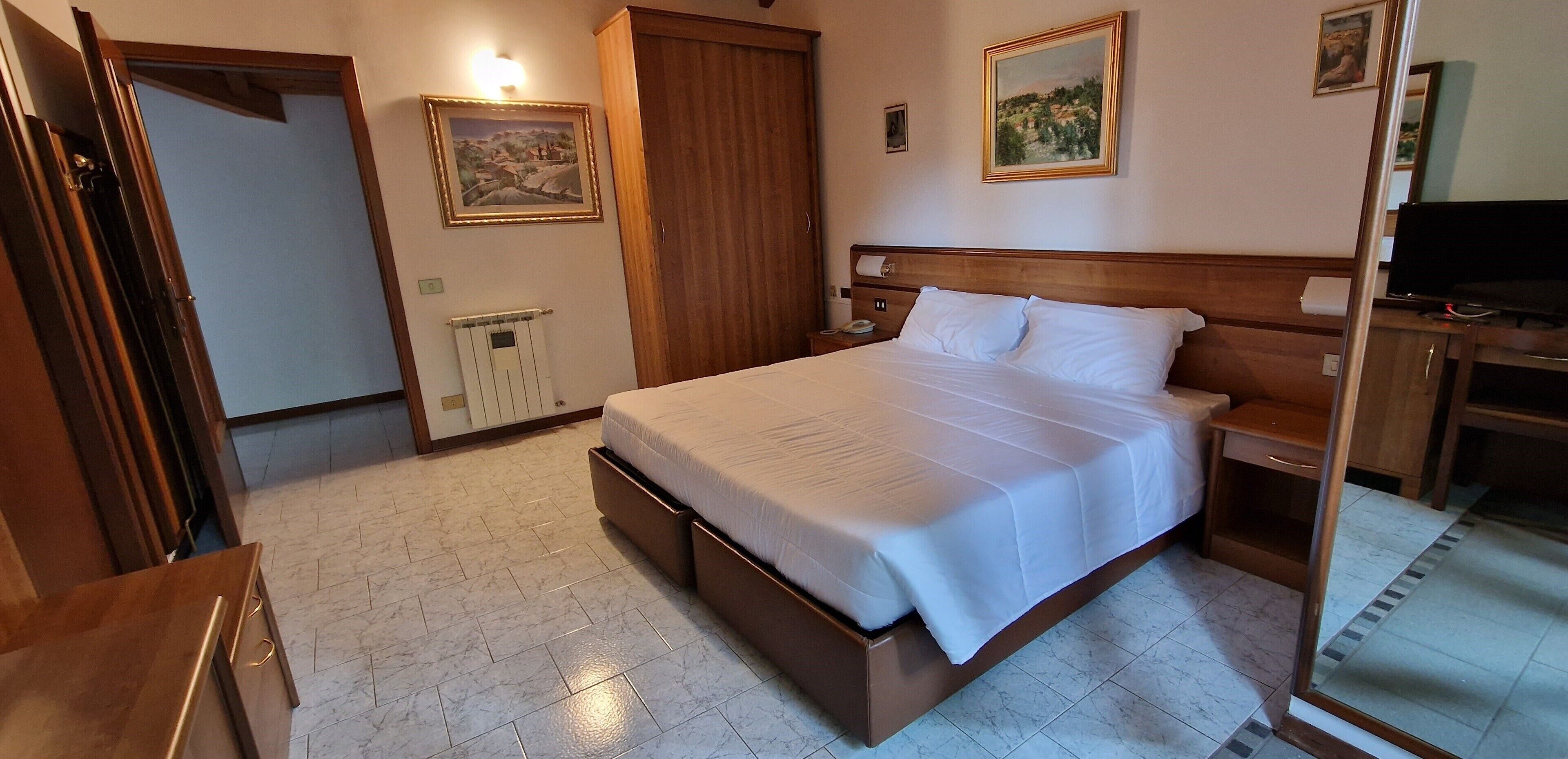 Una habitación de hotel con una cama grande, cabecera de madera, una mesita de noche, un televisor y un armario.