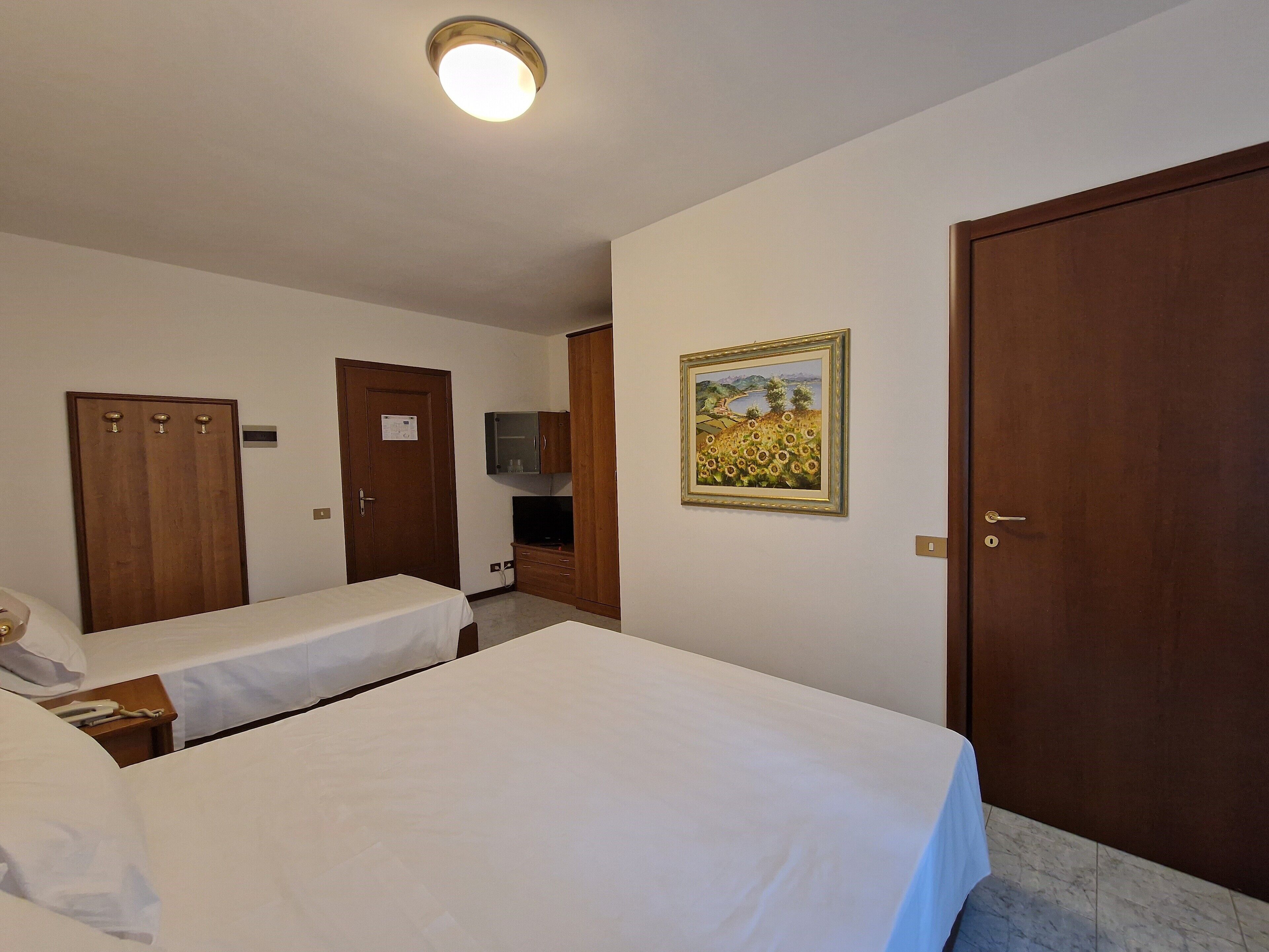 A hotel room with two beds, a wooden wardrobe, a television, and a painting on the wall.