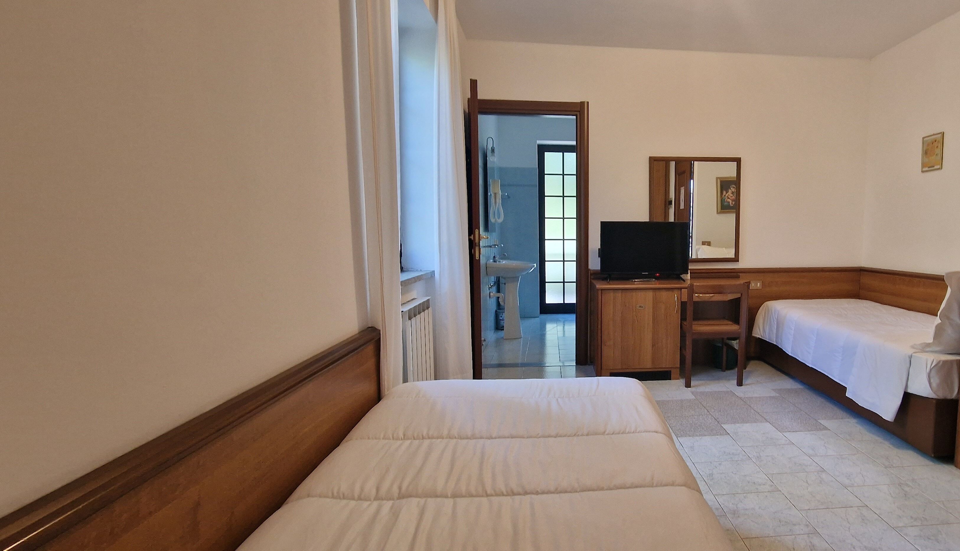 A hotel room with a bed, a desk with a television, a chair, and a small table.