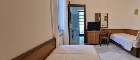 A hotel room with a bed, a desk with a television, a chair, and a small table.
