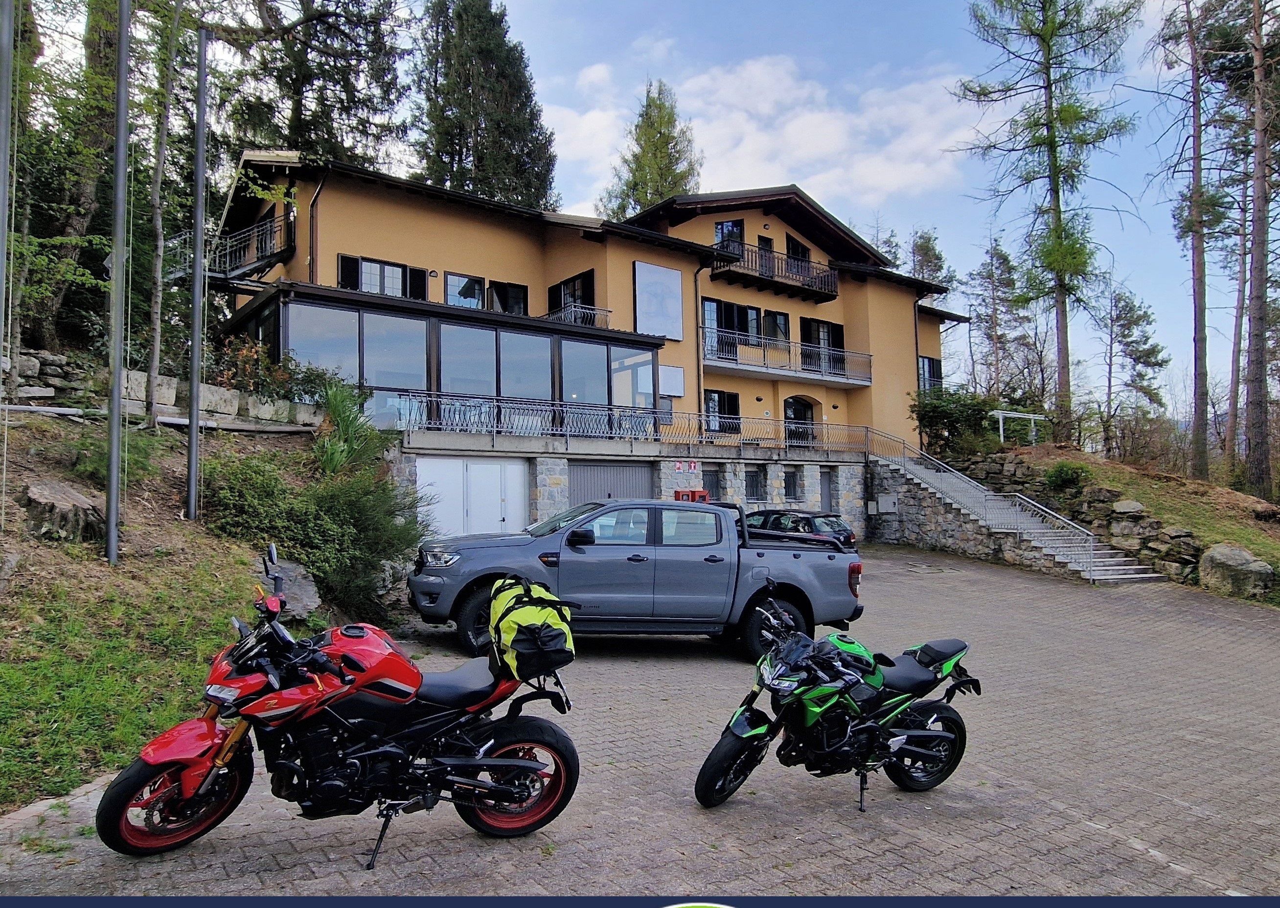 A building with a stone staircase and a parked SUV. There are two motorcycles in front of the building. The image also includes a sign for free EV charging and a bicycle symbol.
