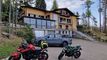 A building with a stone staircase and a parked SUV. There are two motorcycles in front of the building. The image also includes a sign for free EV charging and a bicycle symbol.