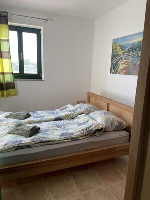 A single bed with a wooden headboard, a window with a curtain, and a painting on the wall.