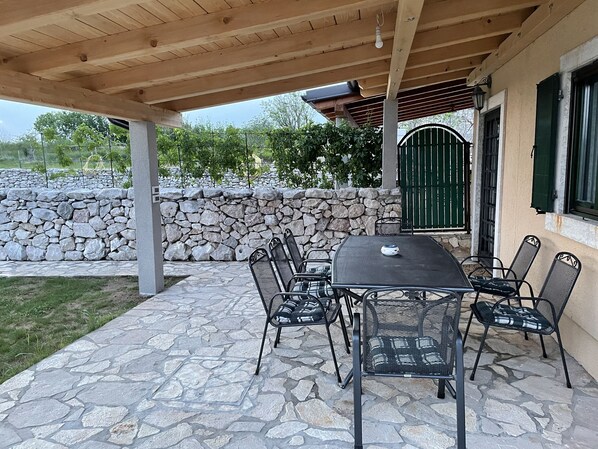An outdoor patio with a stone floor, a wooden pergola, and a table with chairs.